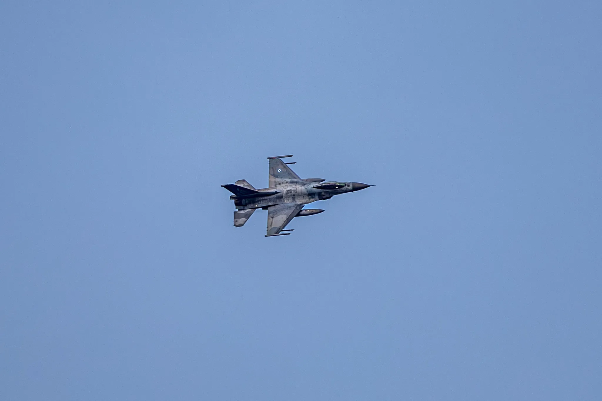 Eine F-16 Fighting Falcon in steiler Schräglage, Rumpfunterseite und Tragflächen deutlich vor wolkenlosem blauem Himmel zu erkennen.