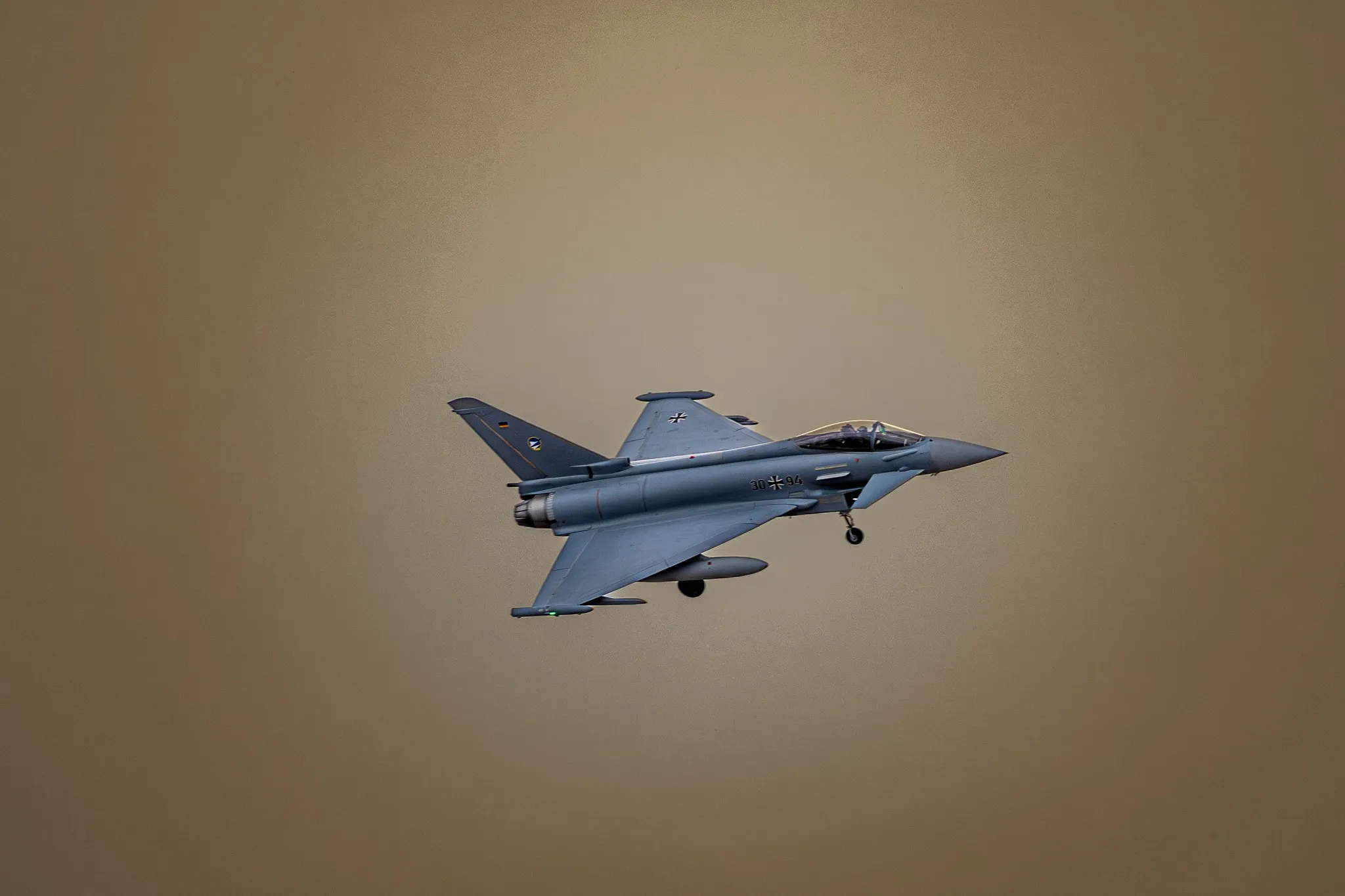 Ein Eurofighter Typhoon der deutschen Luftwaffe im Kurvenflug mit ausgefahrenem Fahrwerk vor goldbraun getöntem Himmel.