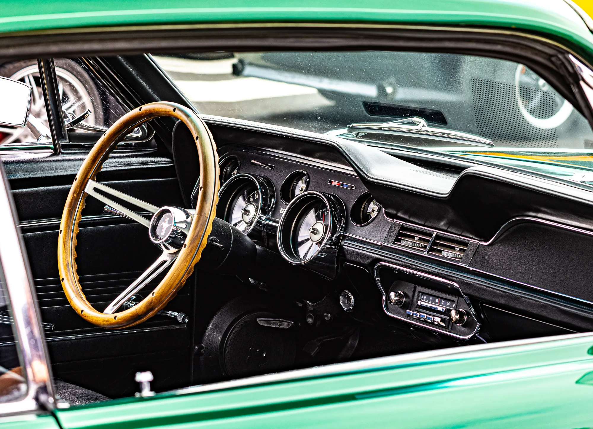Blick durch die Fahrertür eines grünen 1968er Ford Mustang auf das Cockpit mit Holzlenkrad, verchromten Rundinstrumenten und Original-Radio.